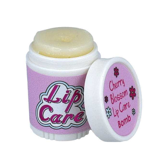 Lip care product in a container featuring a twist-off cap. The container is predominantly pink with the words "Lip Care" in bold, colorful lettering on the front. The cap is slightly open, revealing a pale yellow lip balm inside. Next to it, a smaller lid displays the text "Cherry Blossom Lip Care Bomb" along with a floral design. The overall design suggests a playful and soothing lip care product.